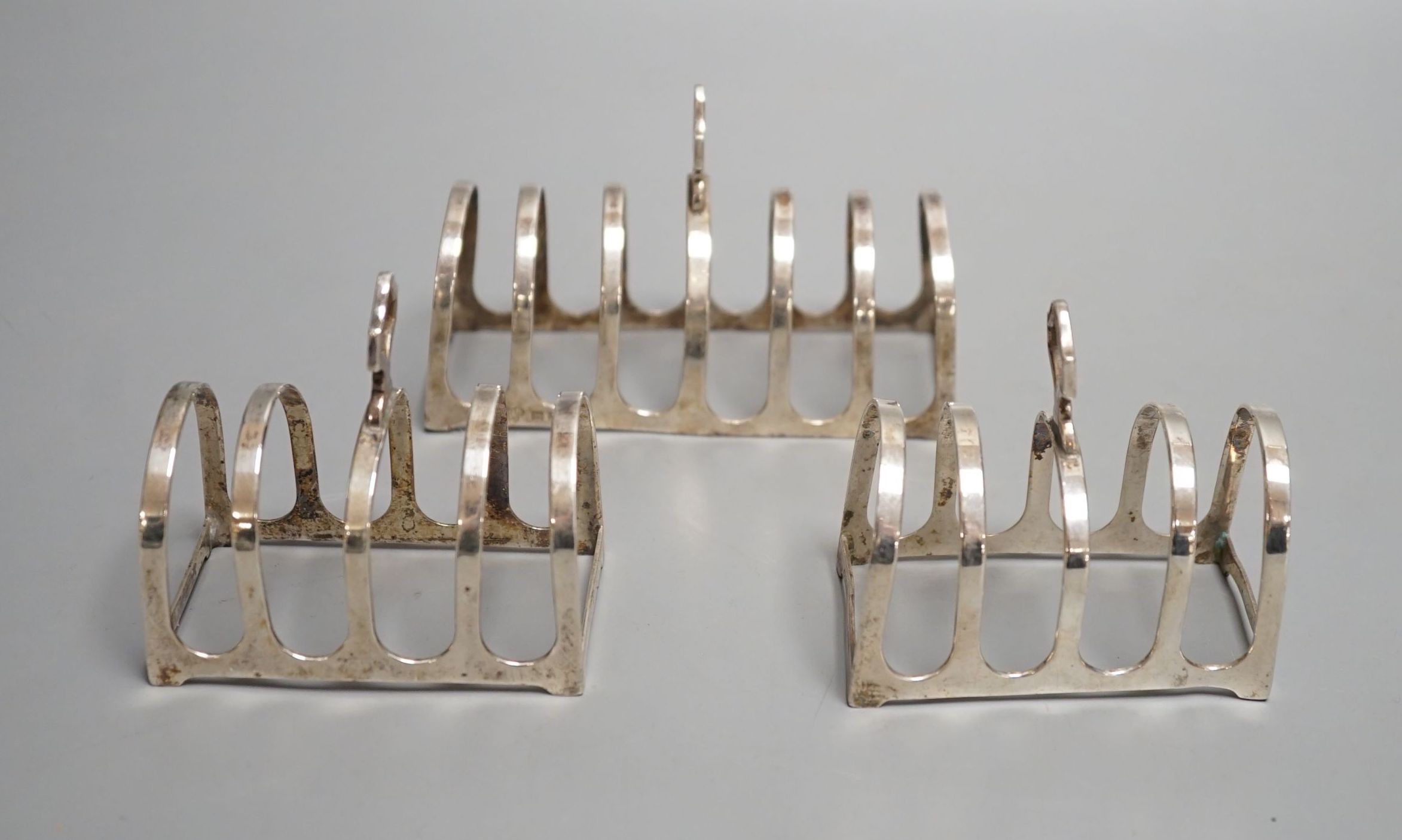 A matched suite of three silver toastracks, pair by Adie Bros. Birmingham, 1934 and larger by Goldsmiths & Silversmiths, London, 1934, 11.2cm, 162 grams.